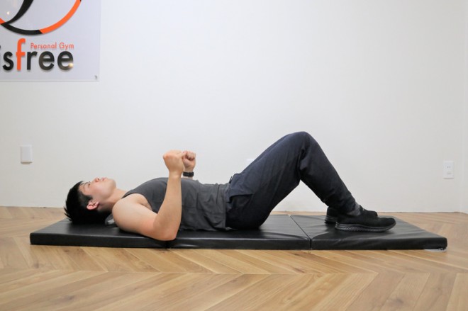 背筋を鍛える際の僧帽筋を鍛えるリバースエルボープッシュアップの動作　１．膝を立てて仰向けに寝転び、肘を地面につける。